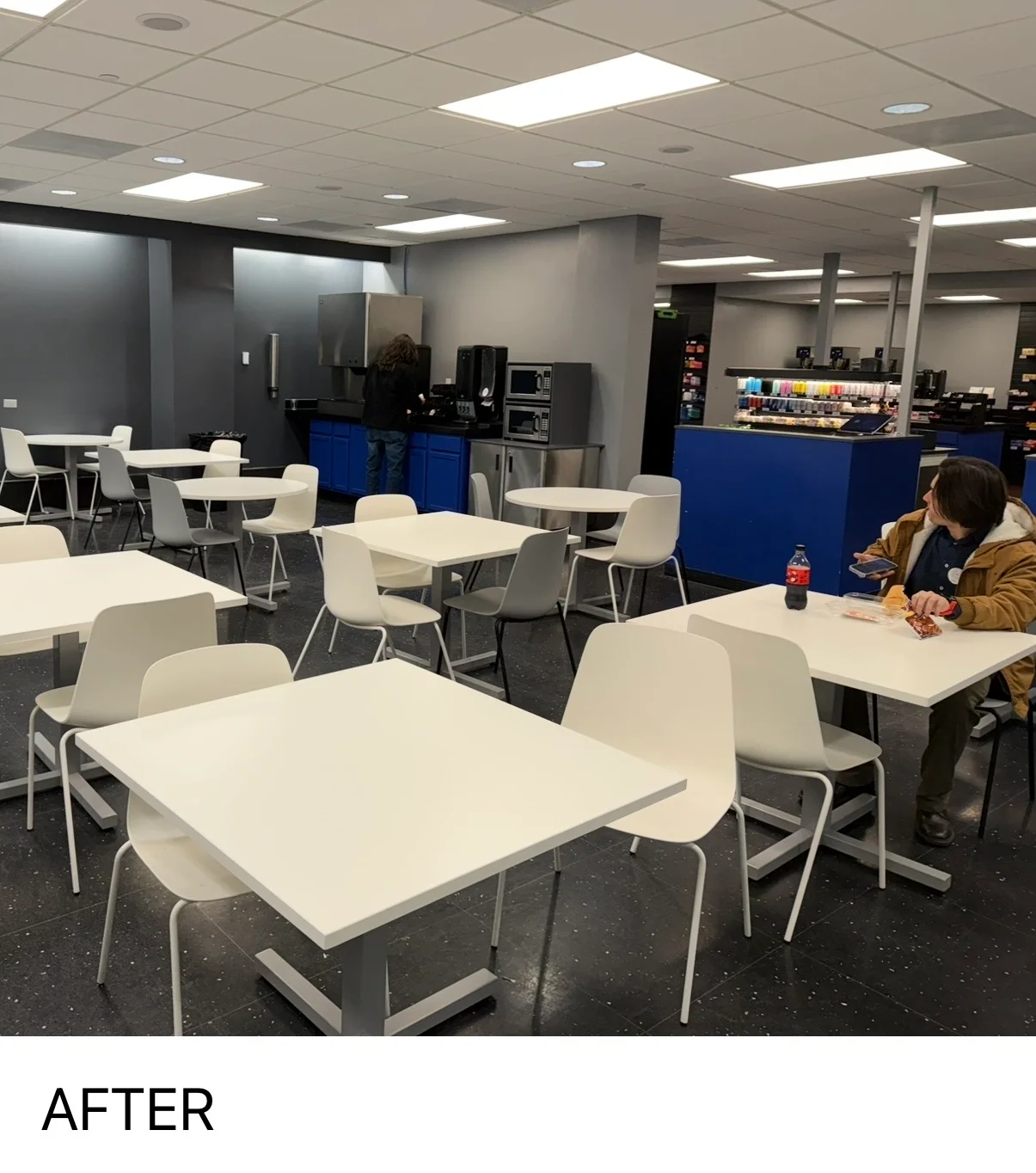 Modern commercial break room with painted walls, white furniture, and blue kitchen cabinetry