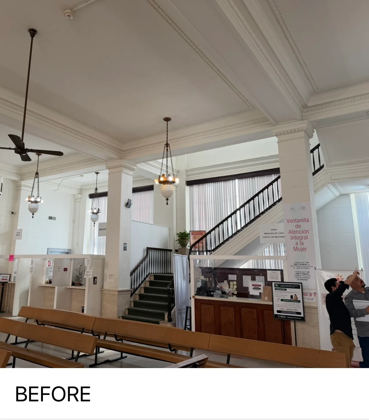 Historic interior with painted coffered ceiling, white walls, black staircase railing, and pendant lighting