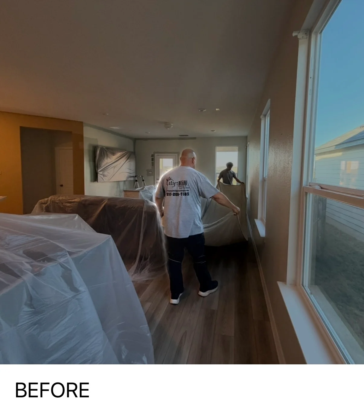Interior painting project with furniture protected by plastic sheeting and workers applying paint